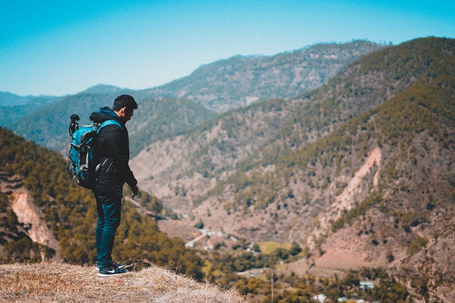 man in jacket and with backpack standing on a mountain