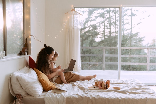 woman and small girl using laptop on bed